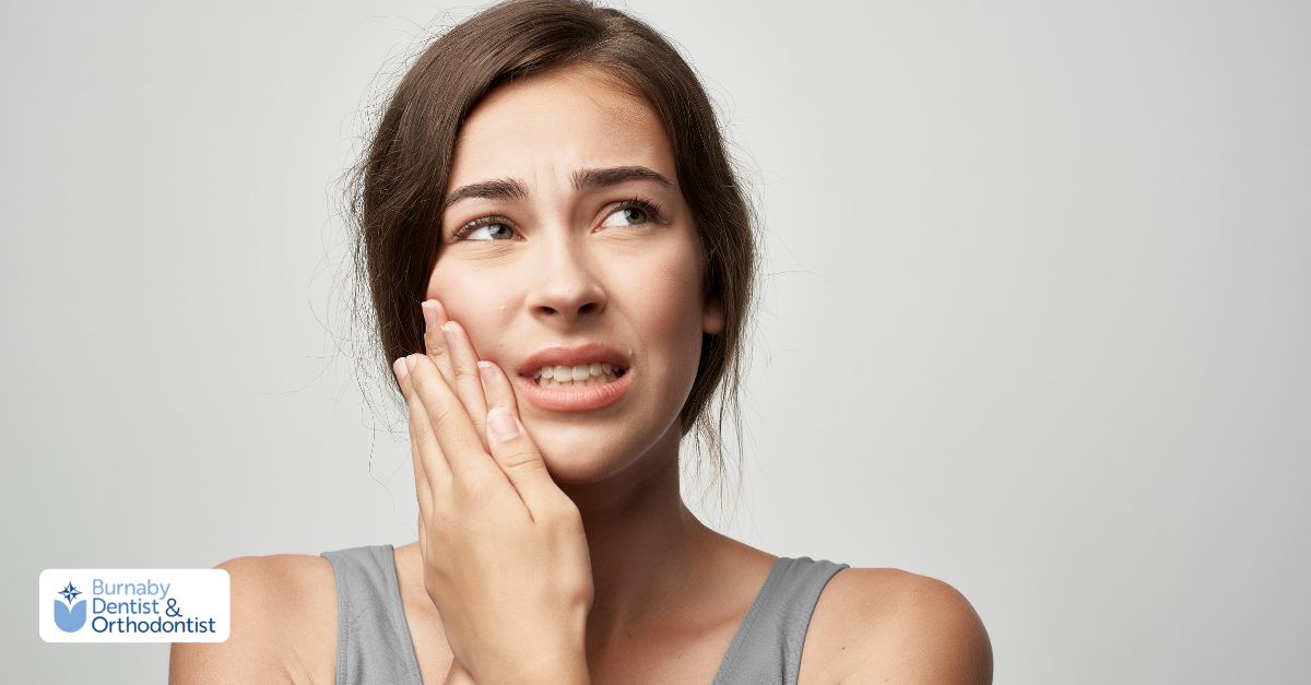 A woman grimaces in pain, holding her jaw, indicating pain after a tooth extraction.