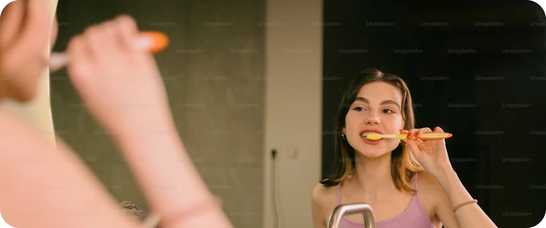 Woman smiling in front of a mirror while brushing teeth with whitening paste.
