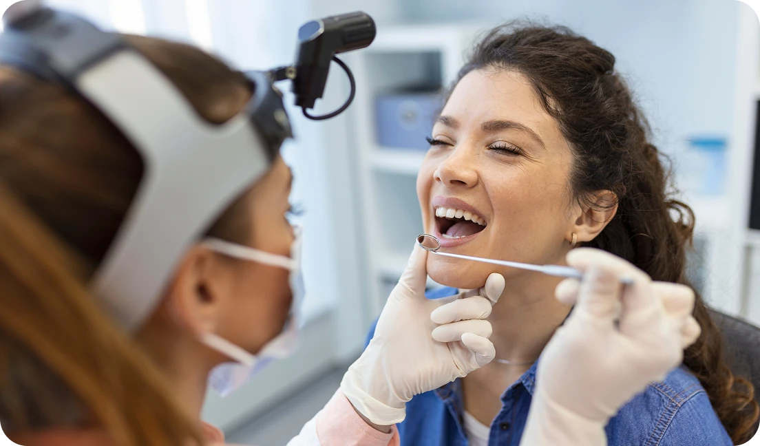 Female dentist examining a woman’s teeth with a dental mirror during checkup