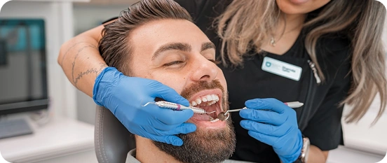 Dentist examining male patient’s teeth with dental instruments.