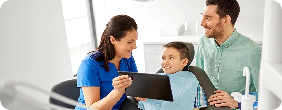 Dentist showing a young boy dental information on a tablet during a checkup.