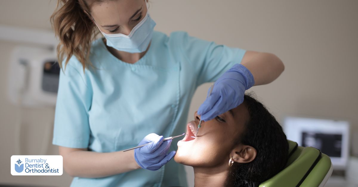 A woman in a dentist chair listens to a man speaking to her about her treatment in an emergency family dentistry clinic. 