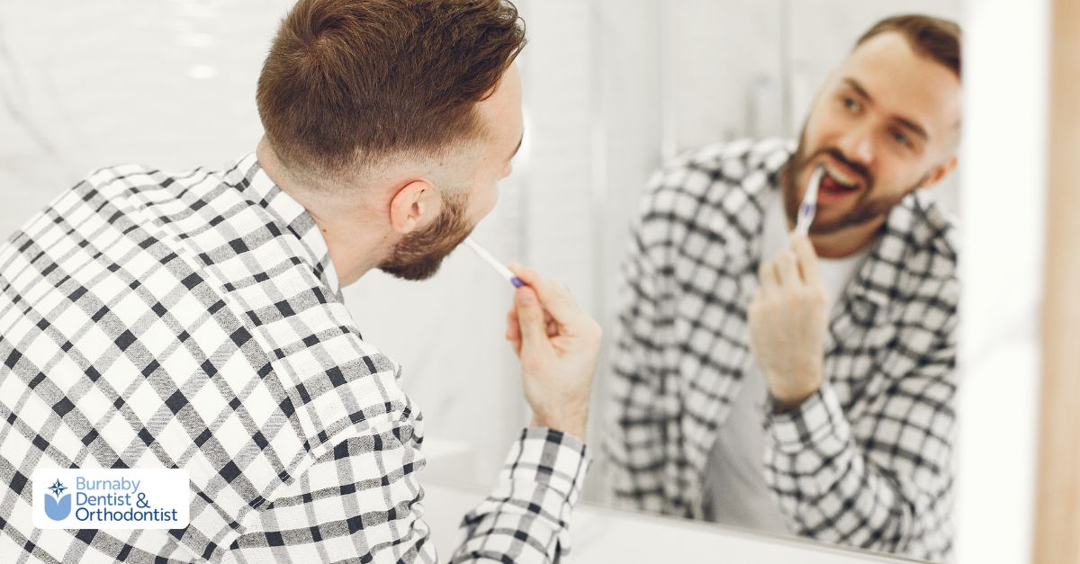 A man in front of a mirror brushing his teeth, emphasizing aftercare for his cosmetic dental bridge.