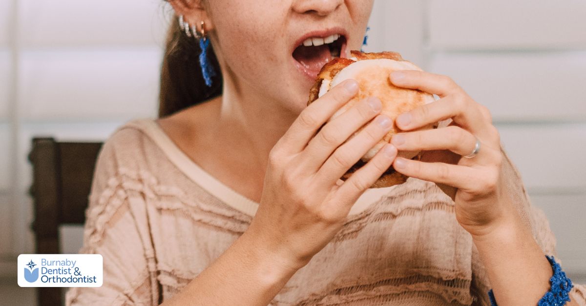 Person attempting to bite into a burger, illustrating when it is safe to resume a normal diet after gum grafting